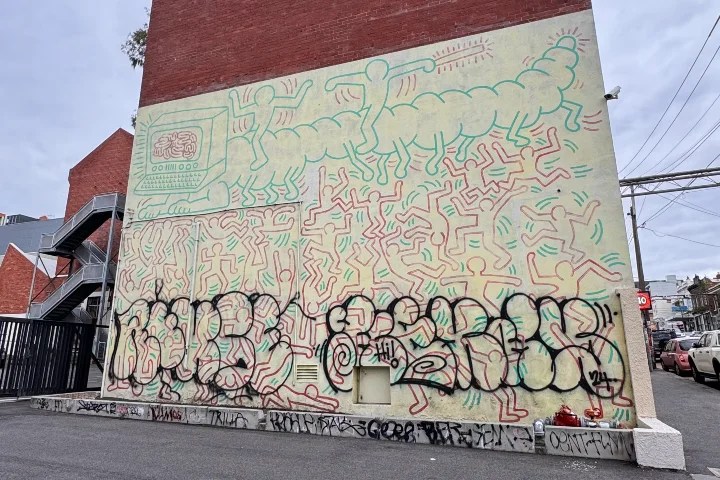 A colorful street mural featuring abstract human figures and a computer, set against a brick wall in Collingwood, Melbourne.
