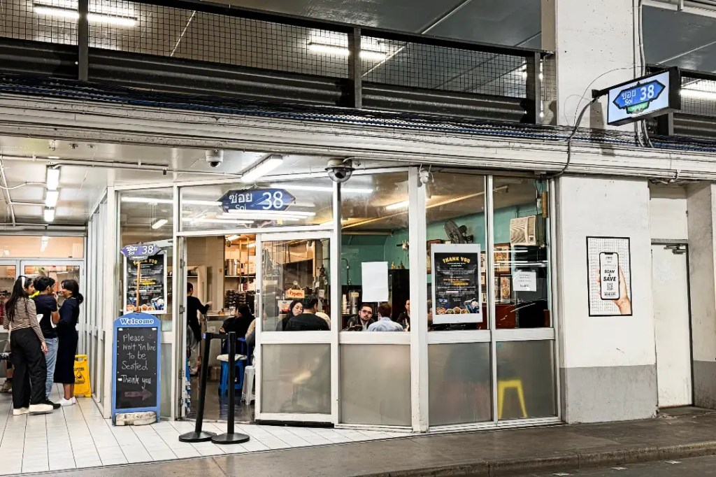 Exterior view of Soi 38, a popular restaurant in Melbourne's CBD at its original location inside a carpark, featuring a welcoming entrance with a sign displaying its name and a queue of diners waiting to be seated.