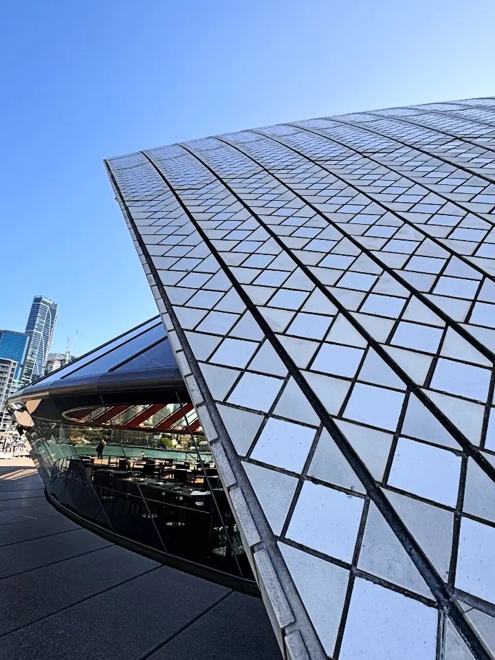 Close-up view of the Sydney Opera House's tiled exterior, showcasing its unique architectural design against a bright blue sky.