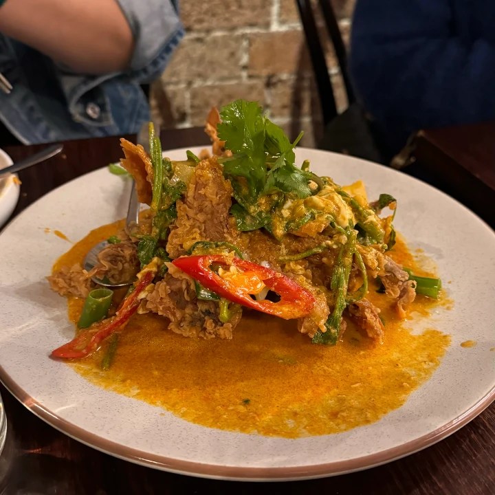 A vibrant dish featuring crispy soft shell crab topped with red chili slices and fresh coriander, served on a plate with a yellow curry sauce.