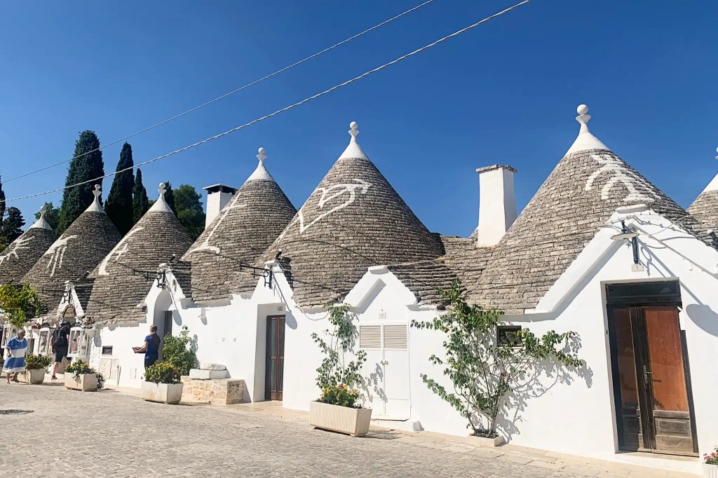 A row of traditional trulli houses with conical roofs, set against a clear blue sky, in the charming town of Alberobello, Italy.