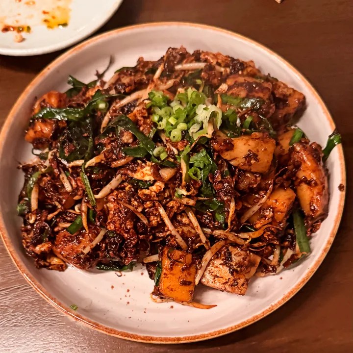 A close-up of a plate of Singaporean fried carrot (turnip) cake garnished with bean sprouts and scallions.
