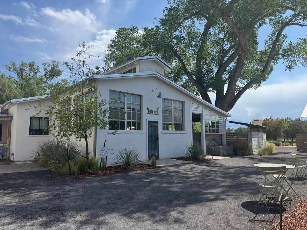 Exterior view of Campo at Los Poblanos, featuring a white building surrounded by greenery and outdoor seating.