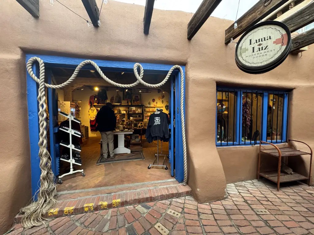 Entrance of Luna Luz shop featuring a rustic adobe exterior, blue door frames, and merchandise displays outside.