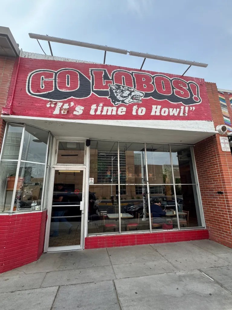Exterior view of a restaurant with a red and white sign that reads 'GO LOBOS! It's time to Howl!' showcasing a vibrant urban setting.