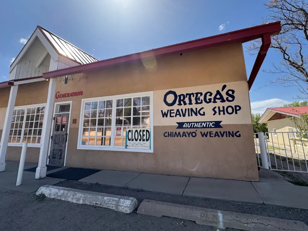 Exterior view of Ortega's Weaving Shop, featuring a sign that reads 'CLOSED'. The building has a stucco finish and large front windows.