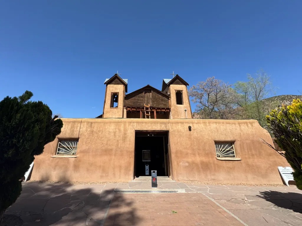 The Santuario de Chimayó in Ranchos de Taos, showcasing its adobe architecture against a clear blue sky.