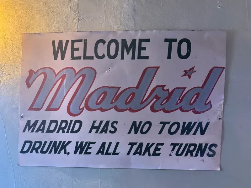 Welcome sign for the town of Madrid, New Mexico, featuring humorous text about community drinking.