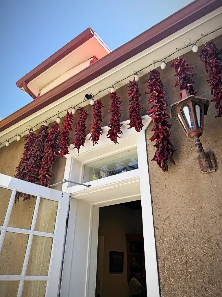 Exterior view of a restaurant with drying red chilies hanging above the door, against a clear blue sky.
