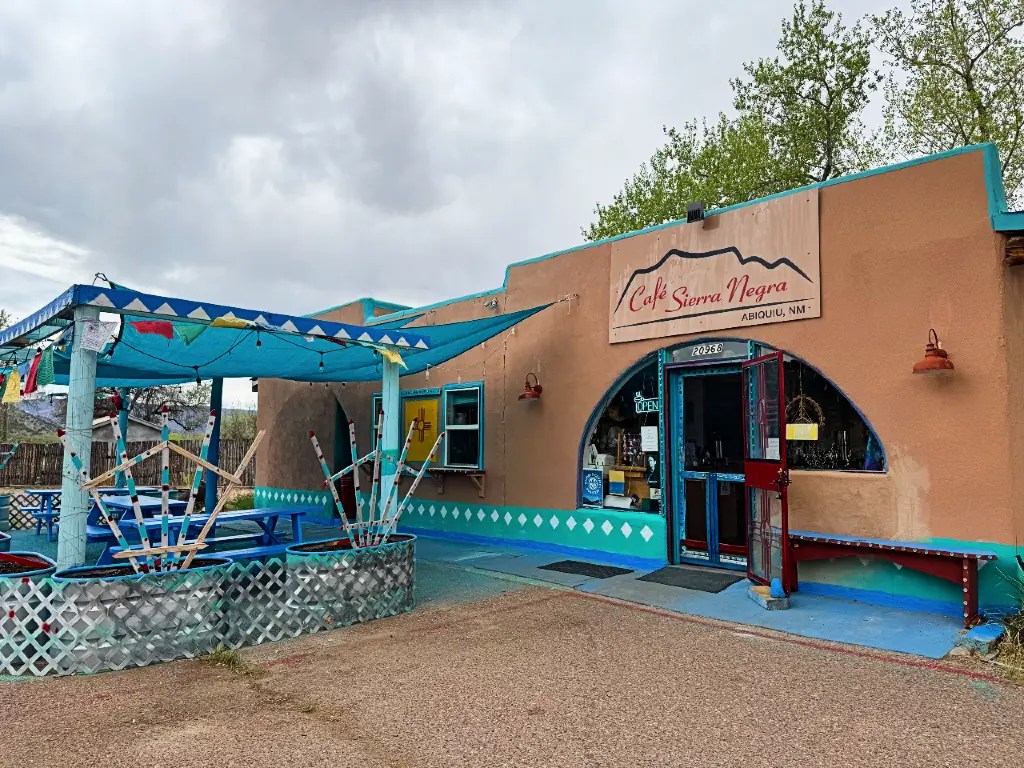Exterior view of Cafe Sierra Negra in Abiquiu, NM, featuring a turquoise awning, colorful decorations, and an inviting outdoor seating area.
