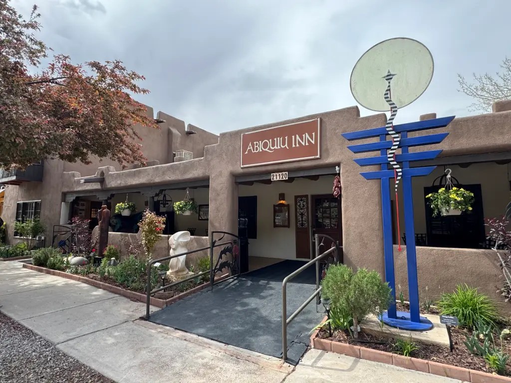 Exterior view of Abiquiú Inn, featuring adobe-style architecture, a prominent sign, and decorative elements including sculptures and plants.