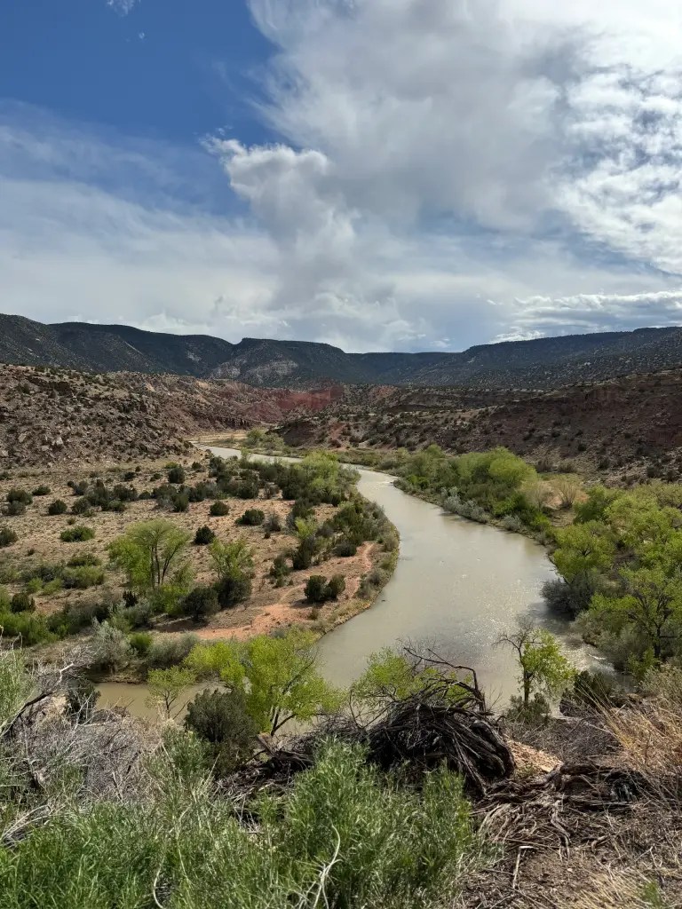 Scenic view of a winding river surrounded by lush greenery and rocky cliffs under a cloudy sky.
