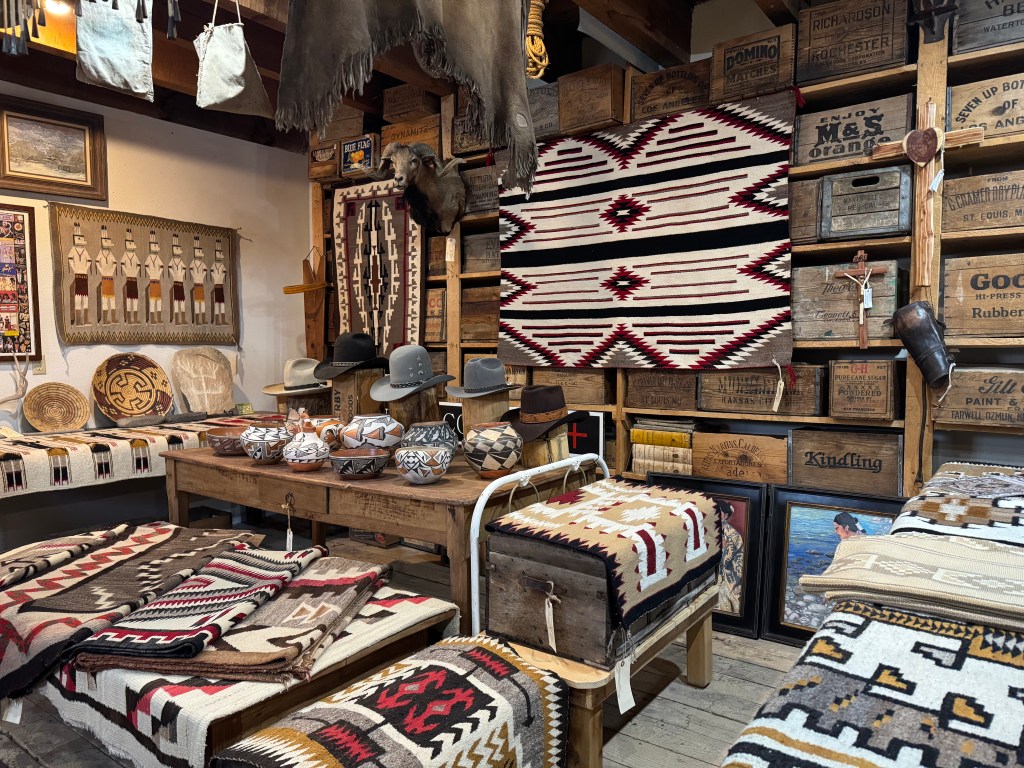 A cozy interior showcasing an assortment of woven blankets, pottery, hats, and wooden crates, reflecting Southwestern and Native American artistry.