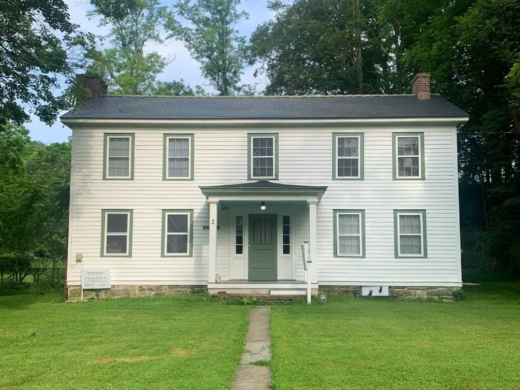 White two-story house with green trim, surrounded by trees and grass, serving as on-campus housing at Peters Valley School of Craft.