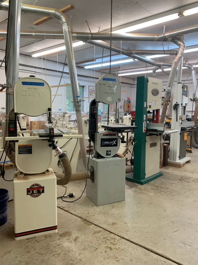 A woodworking studio featuring various types of machinery including band saws, jointers, and dust collection systems.