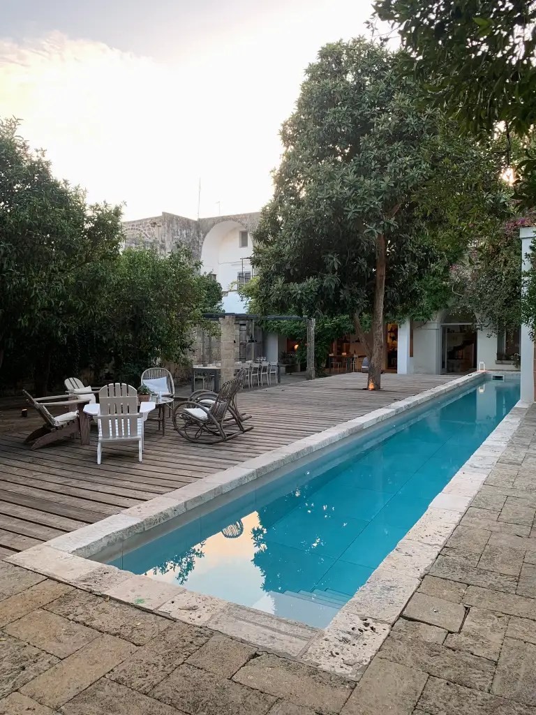 Outdoor view of a villa's pool area surrounded by trees and seating on a wooden deck.