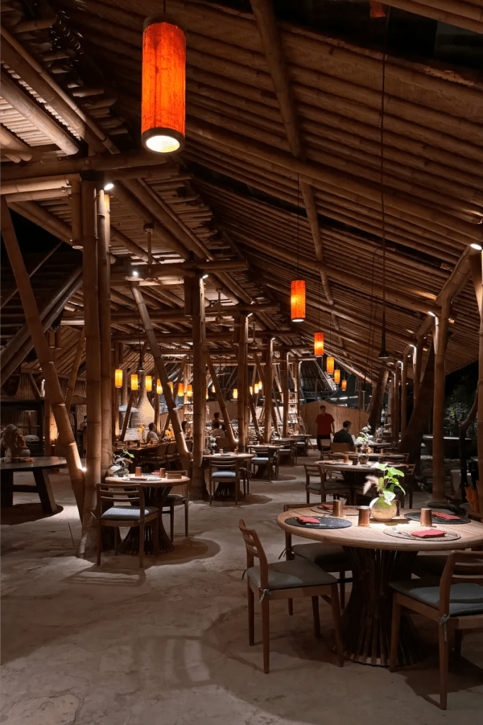 Interior view of a bamboo restaurant in Ubud at night, featuring wooden beams, warm hanging lights, and tables set for dining.