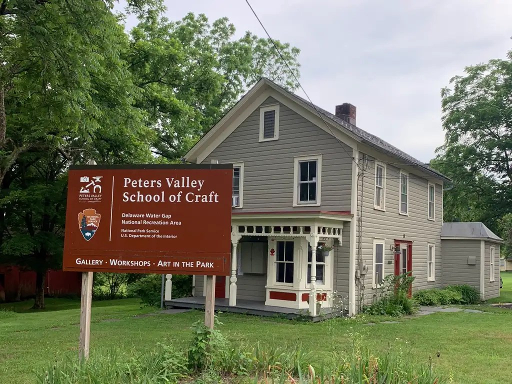 Sign for Peters Valley School of Craft located in the Delaware Water Gap National Recreation Area, featuring a gray house and green surroundings.