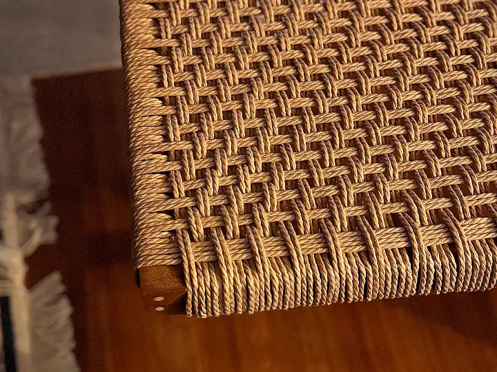 Close-up view of a woven seat made with beige Danish cord, showcasing a detailed weaving pattern and the corner of a wooden frame.