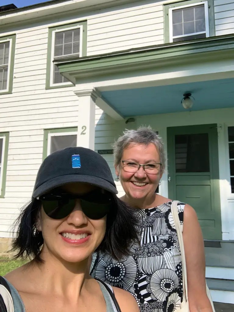 Two women smiling in front of a white house with green trim.