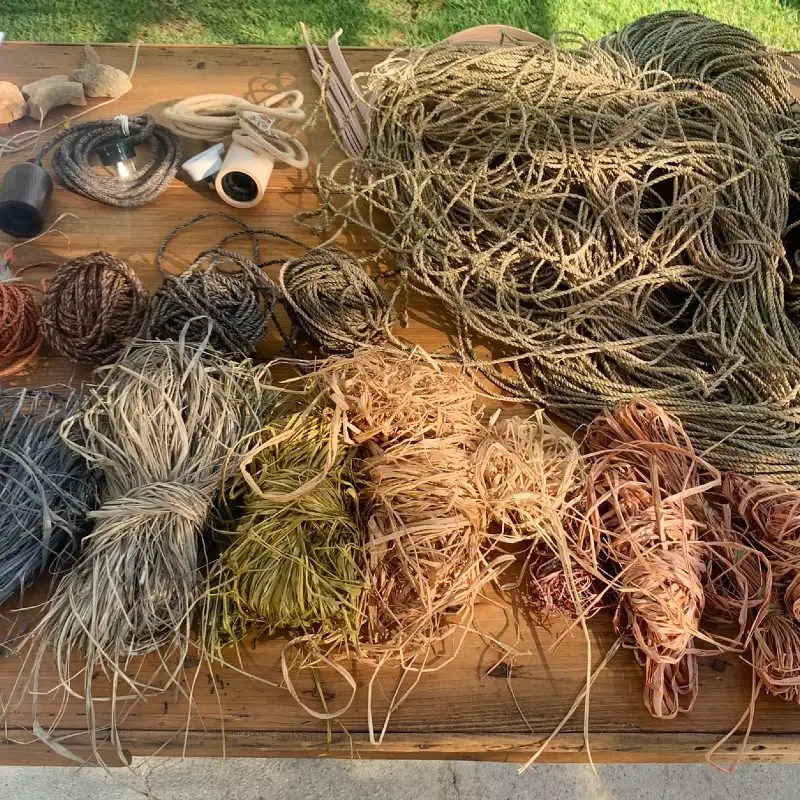 An array of various natural fibers, cords, and materials arranged on a wooden table, showcasing different textures and colors used for crafting.