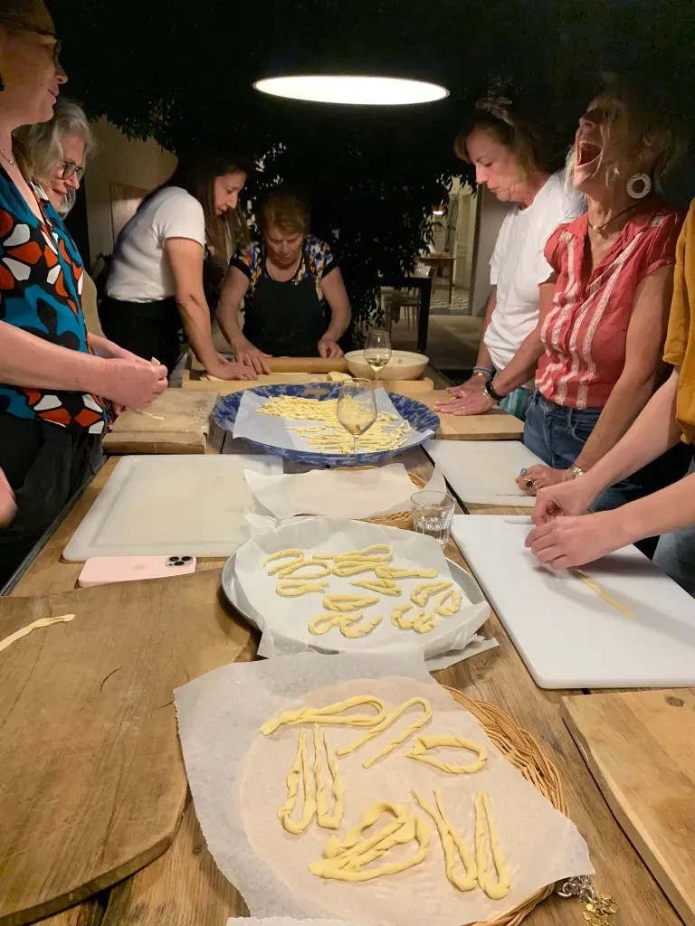 Group of participants engaged in a pasta-making class, working on fresh pasta dough while enjoying camaraderie in a warmly lit kitchen.