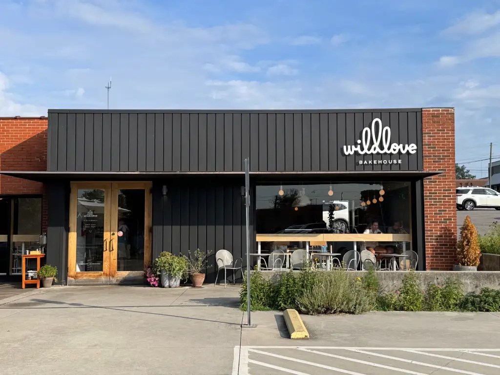Exterior view of Wildlove Bakehouse, showcasing a modern facade with a black and brick design, featuring large windows and outdoor seating.