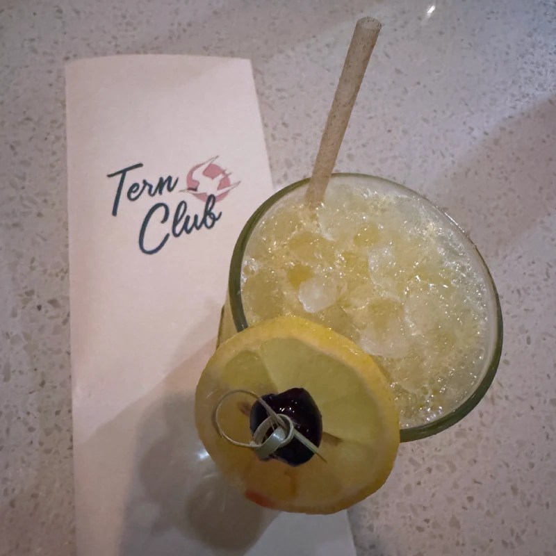 A cocktail served in a glass with a lemon slice and cherry garnish, next to a branded napkin from Tern Club.