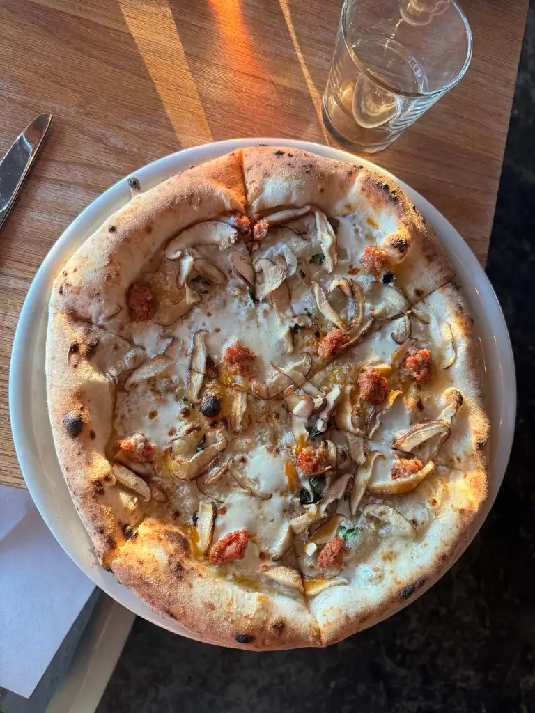 A freshly baked pizza topped with mushrooms and sausage, served on a wooden table next to a glass of water.