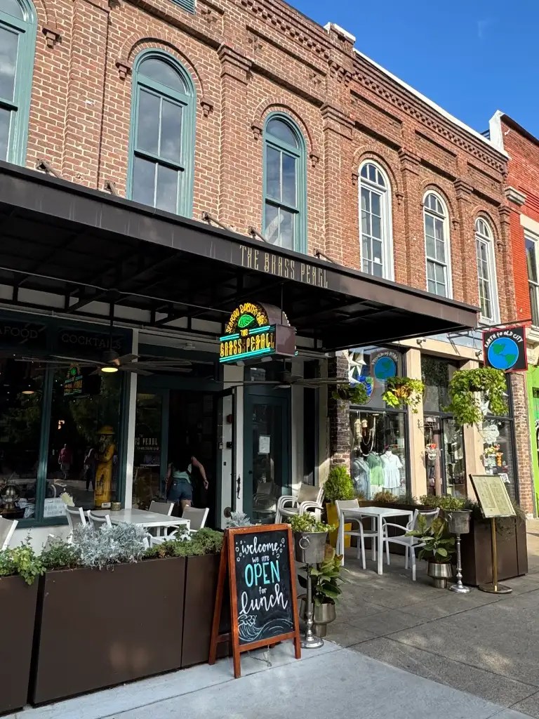 Exterior view of The Brass Pearl restaurant in Knoxville, showcasing its brick facade, outdoor seating, and a sign announcing it is open for lunch.