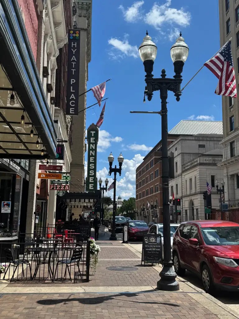 A sunny street view in downtown Knoxville, Tennessee, featuring the Hyatt Place hotel, American flags, and charming storefronts.