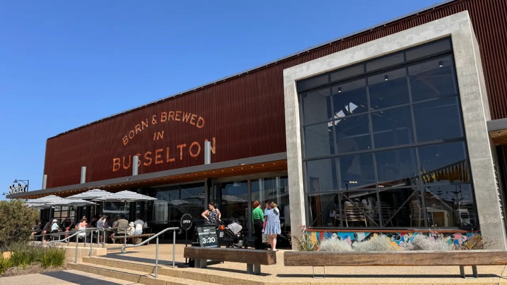 Exterior view of Shelter Brewing in Busselton, featuring a modern building with large glass windows, outdoor seating, and a sign stating 'Born & Brewed in Busselton.'