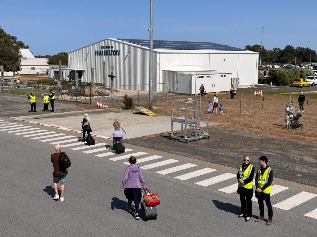 Passengers arriving at Busselton Airport with staff in yellow vests directing traffic and assisting travelers.