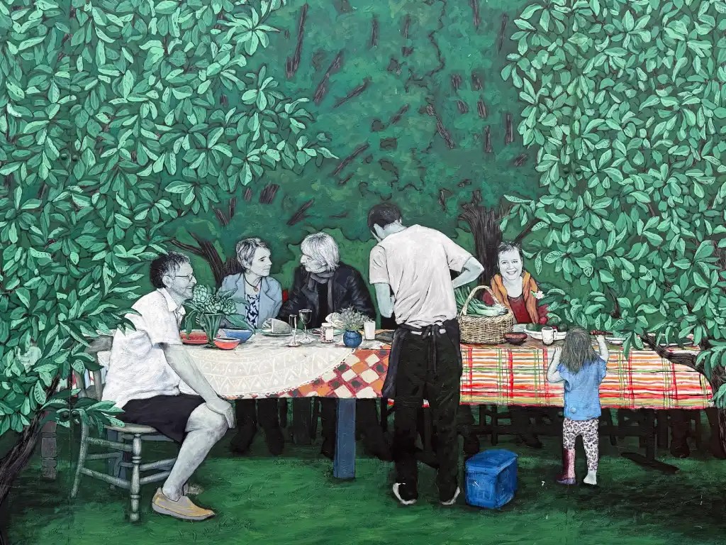 A vibrant mural depicting a group of people sitting around a table in a lush green setting, enjoying a meal and engaging in conversation, with a child playing nearby.
