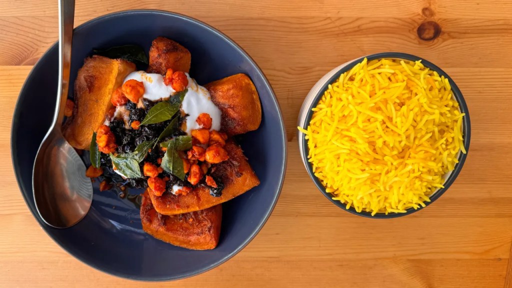 A bowl of spiced squash garnished with yogurt, fried chickpeas, and curry leaves, accompanied by a serving of yellow rice.