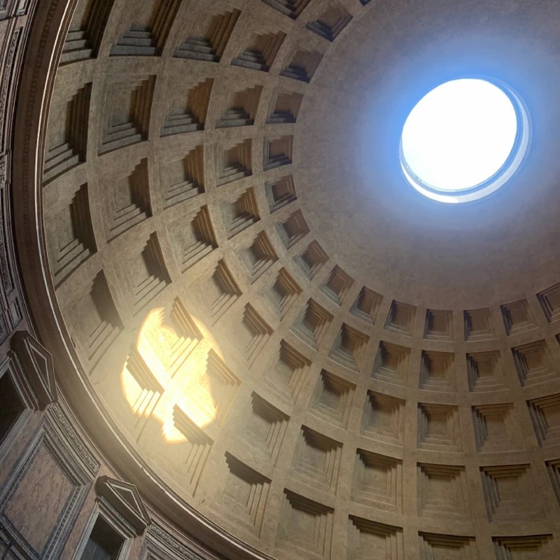 Interior view of the Pantheon dome in Rome, showcasing the oculus and intricate design of the coffered ceiling, with sunlight streaming through.